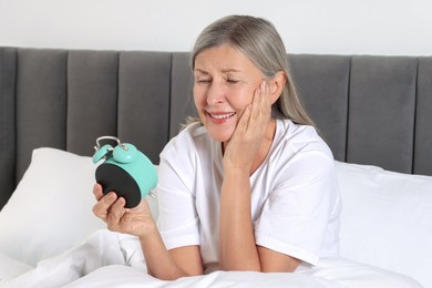 Photo of Overslept woman with alarm clock in bed at home