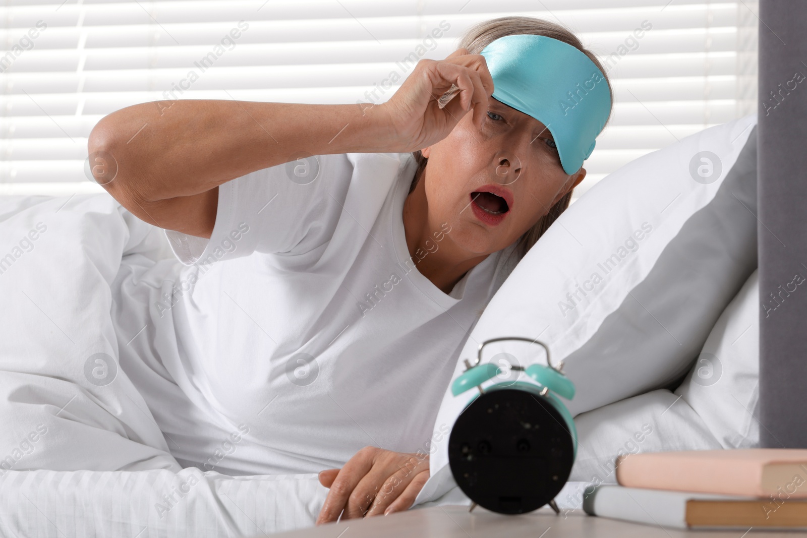 Photo of Overslept woman looking at alarm clock in bed indoors