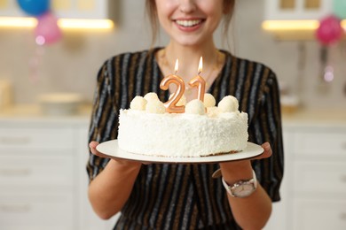 Photo of Coming of age party - 21st birthday. Happy young woman holding tasty cake with number shaped candles at home, closeup