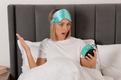 Overslept woman with alarm clock in bed at home