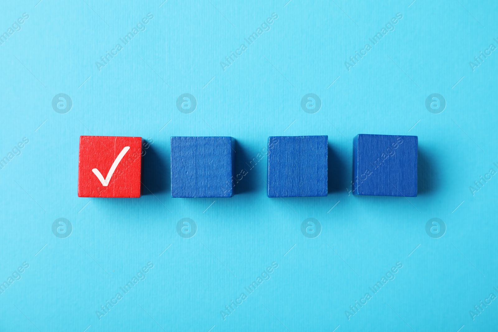 Photo of One red cube with check mark among others on light blue background, flat lay