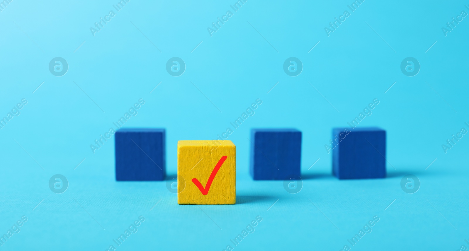 Photo of One yellow cube with check mark among others on light blue background, selective focus