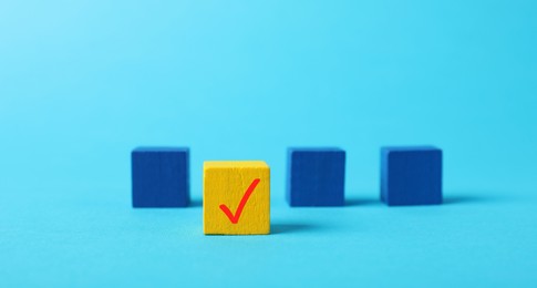 Photo of One yellow cube with check mark among others on light blue background, selective focus