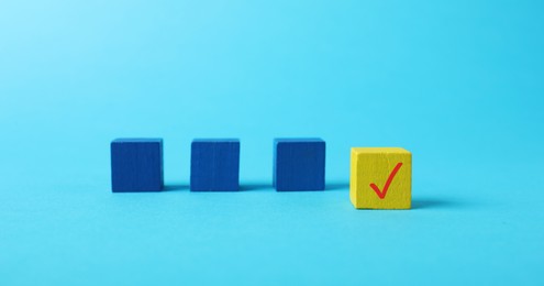 Photo of One yellow cube with check mark among others on light blue background