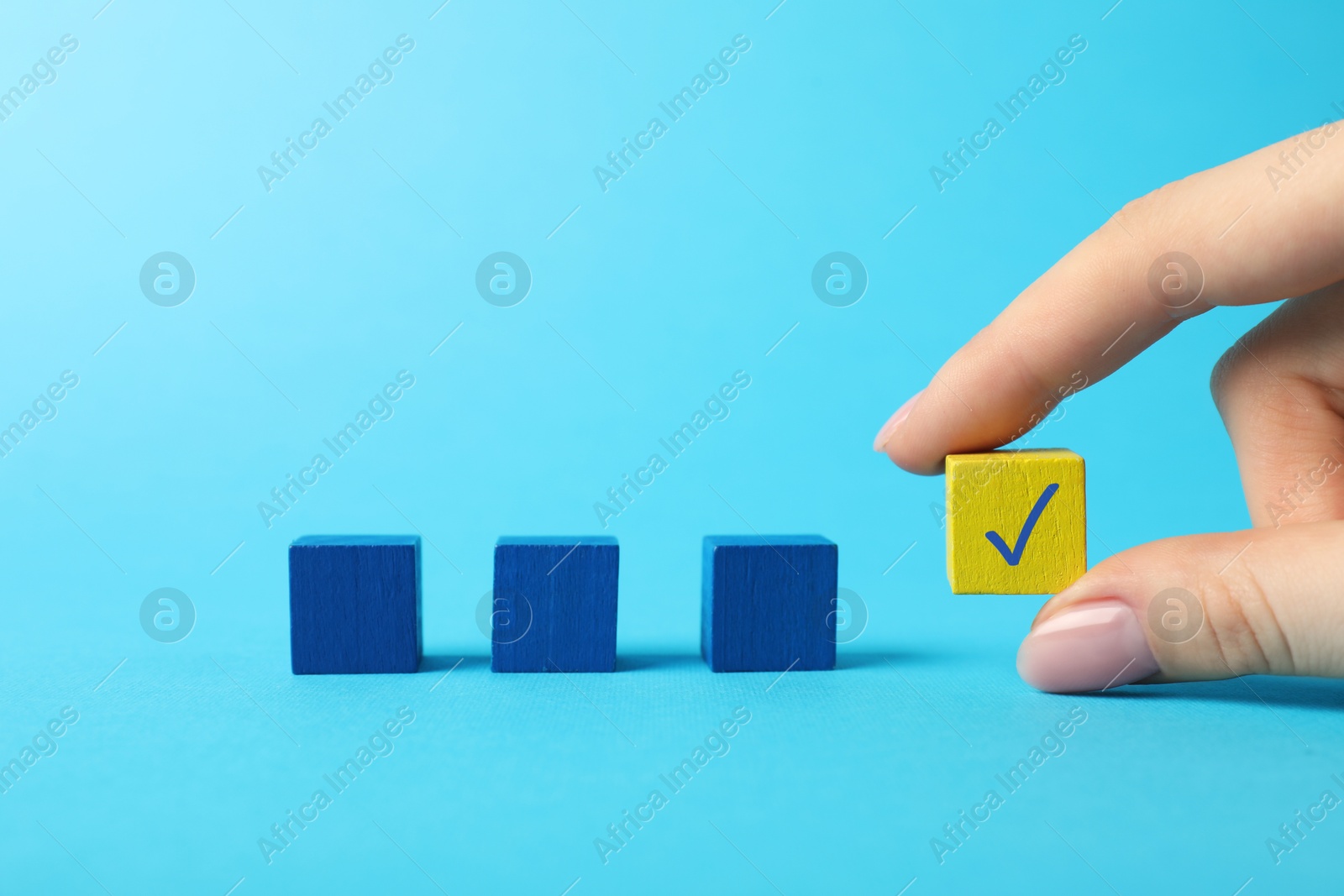 Photo of Woman holding yellow cube with check mark on light blue background, closeup