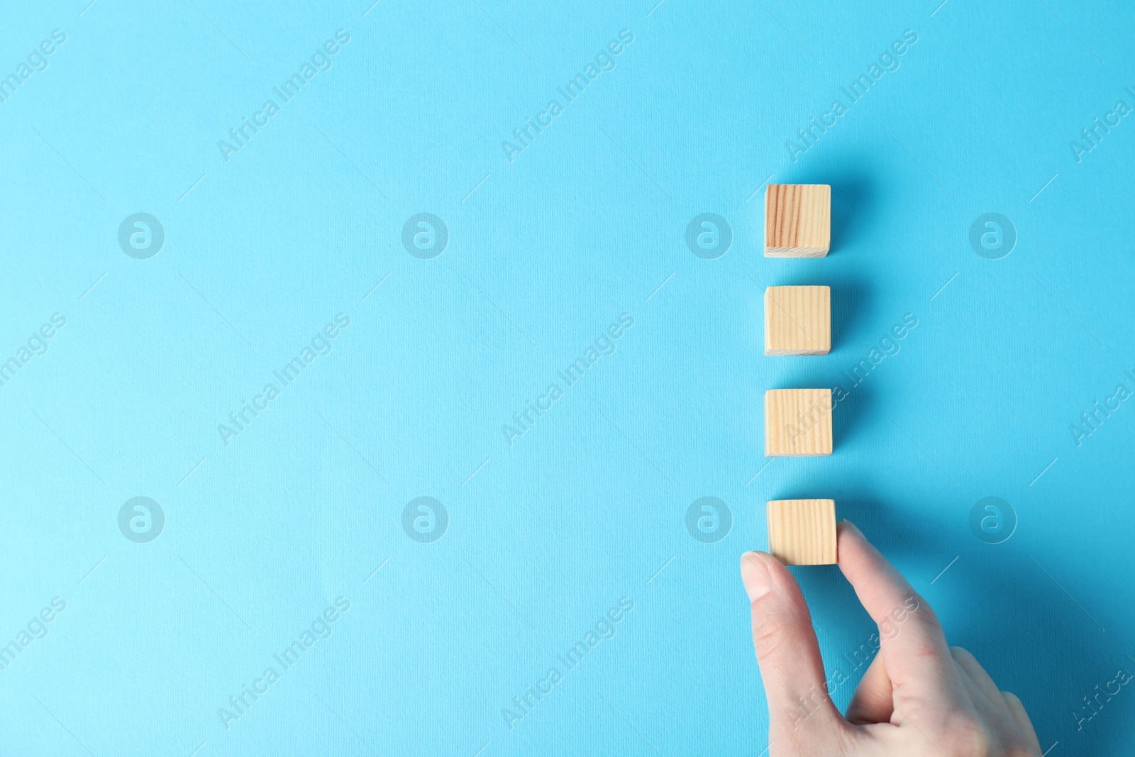 Photo of Woman with wooden cubes on light blue background, top view. Space for text