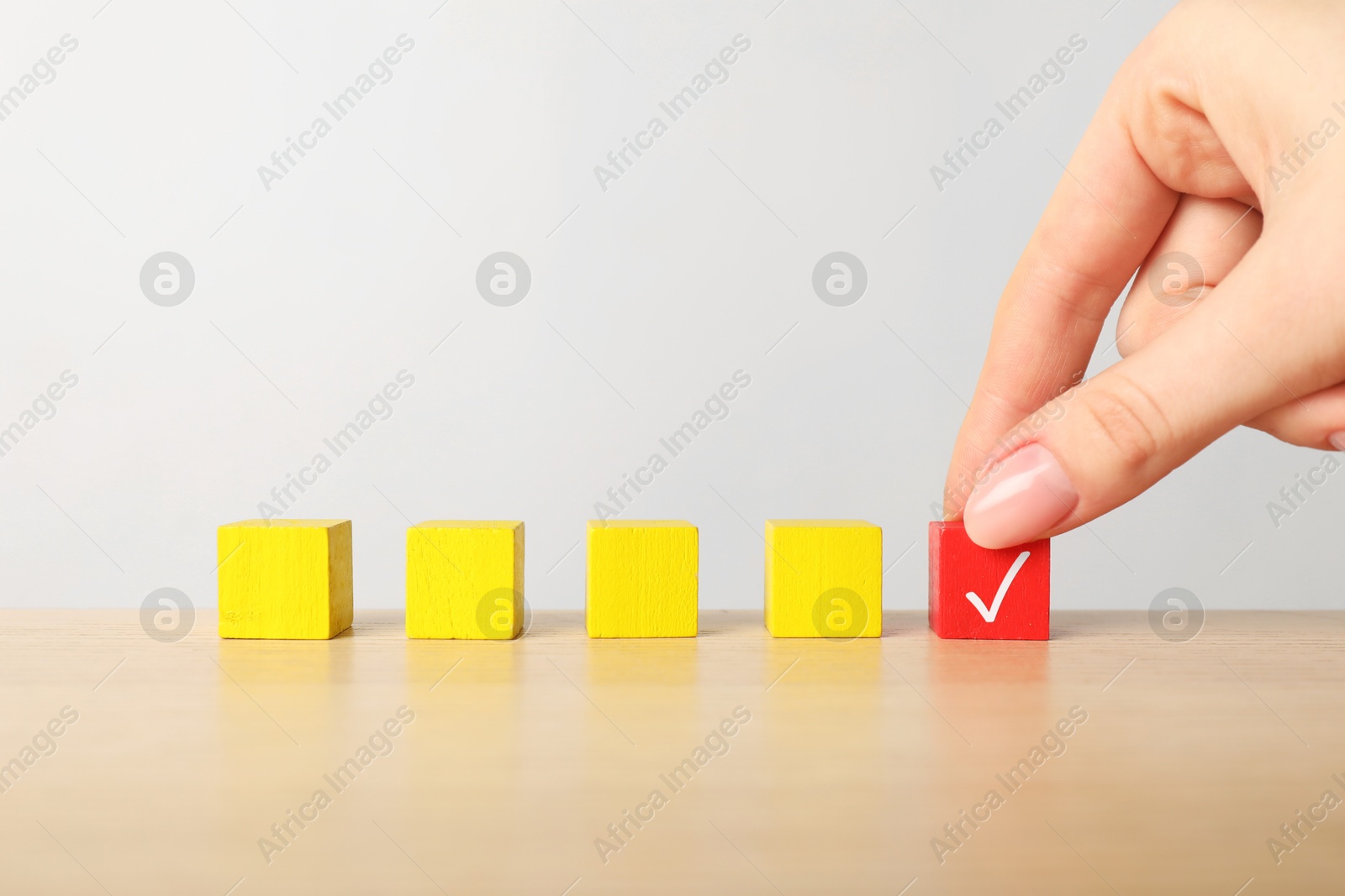 Photo of Woman taking red cube with check mark at table, closeup