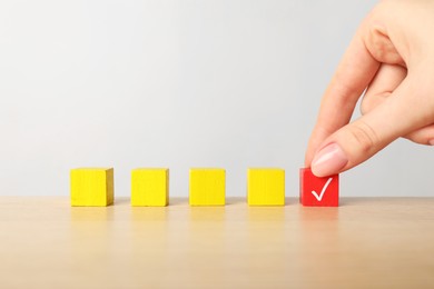 Photo of Woman taking red cube with check mark at table, closeup