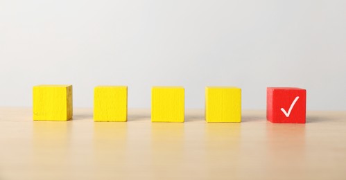 Photo of One red cube with check mark among others on table