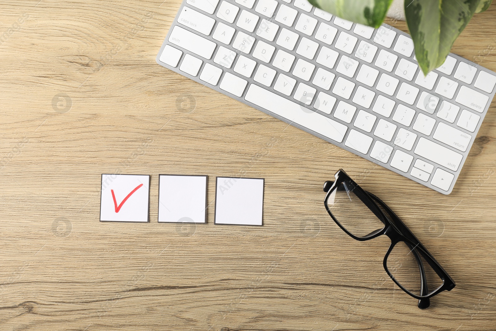 Photo of One checkbox with tick mark among others, computer keyboard, glasses and leaves on wooden table, flat lay