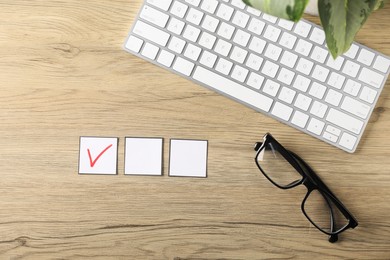 Photo of One checkbox with tick mark among others, computer keyboard, glasses and leaves on wooden table, flat lay