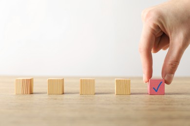 Photo of Woman taking pink cube with check mark at wooden table, closeup