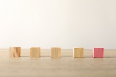 Photo of Many wooden cubes and pink one on table