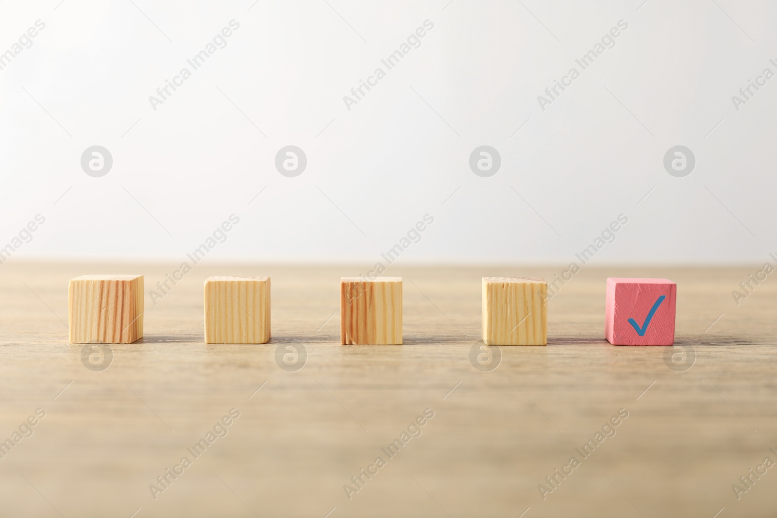 Photo of One pink cube with check mark among others on wooden table