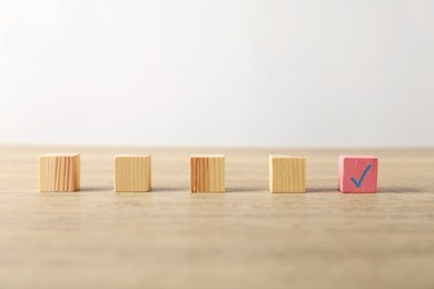 Photo of One pink cube with check mark among others on wooden table