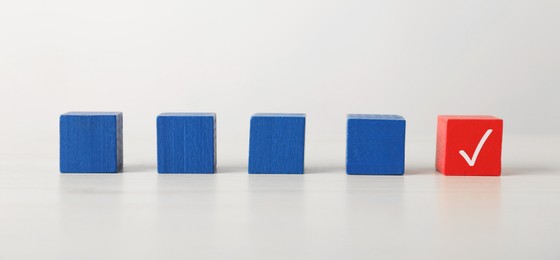 Photo of One red cube with check mark among others on white table