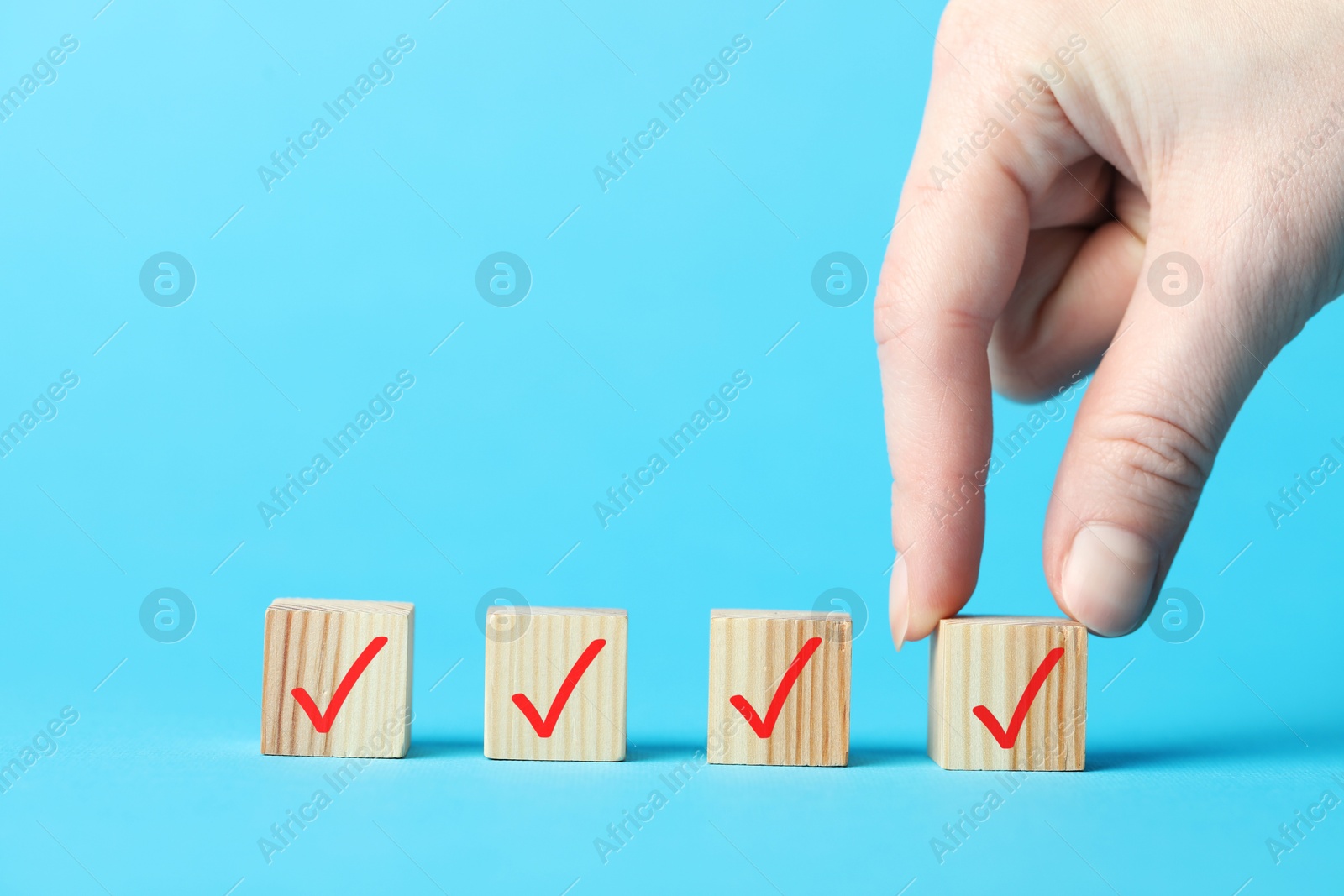 Photo of Woman taking wooden cube with check mark on light blue background, closeup