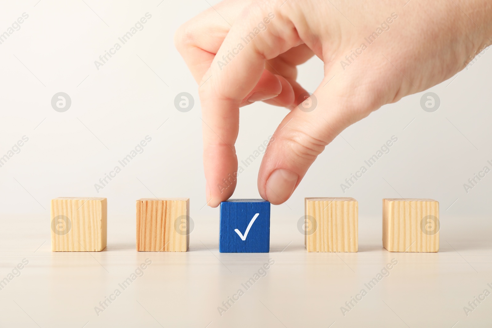 Photo of Woman taking blue cube with check mark at table, closeup