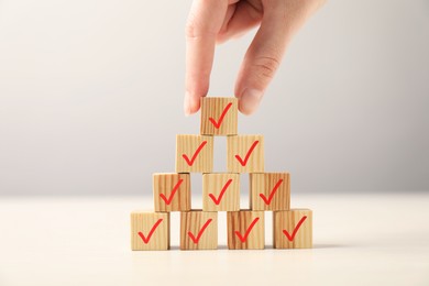 Photo of Woman building pyramid of wooden cubes with check marks at table, closeup