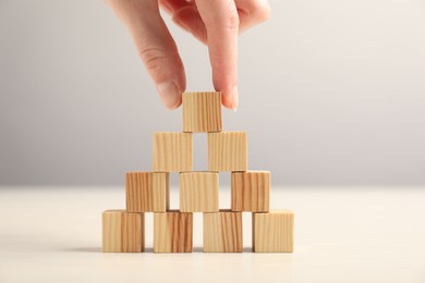 Photo of Woman building pyramid of wooden cubes at table, closeup