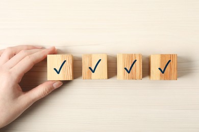 Photo of Woman taking cube with check mark at white wooden table, top view