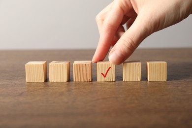 Photo of Woman taking wooden cube with check mark at grey table, closeup