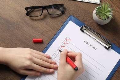 Photo of Woman filling Checklist at wooden table, top view