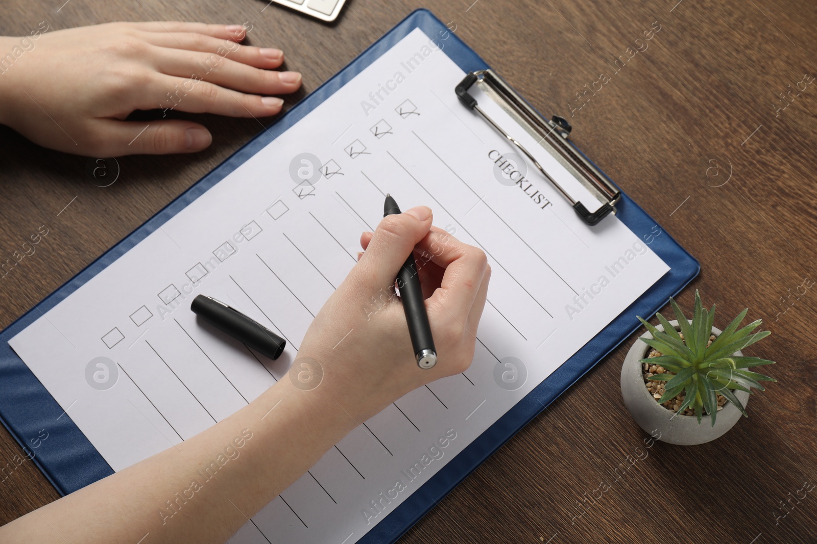 Photo of Woman filling Checklist at wooden table, above view