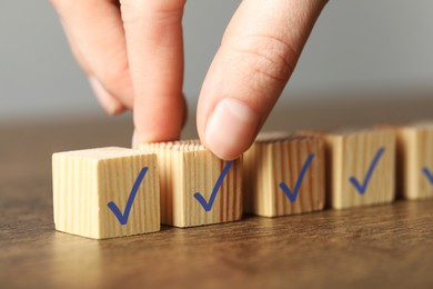 Photo of Woman taking wooden cube with check mark at grey table, closeup