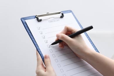 Photo of Woman filling Checklist on blurred background, closeup