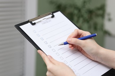 Photo of Woman filling Checklist with pen indoors, closeup