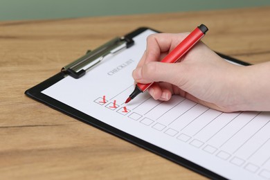 Photo of Woman filling Checklist with marker at wooden table, closeup