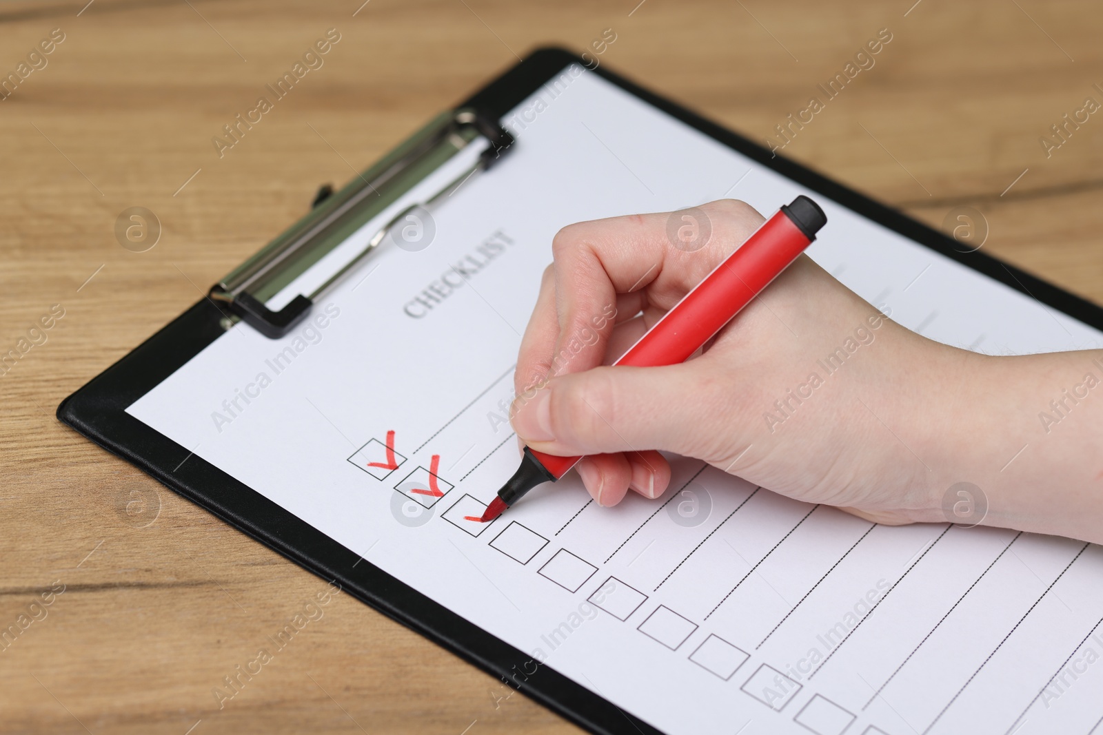 Photo of Woman filling Checklist with marker at wooden table, closeup