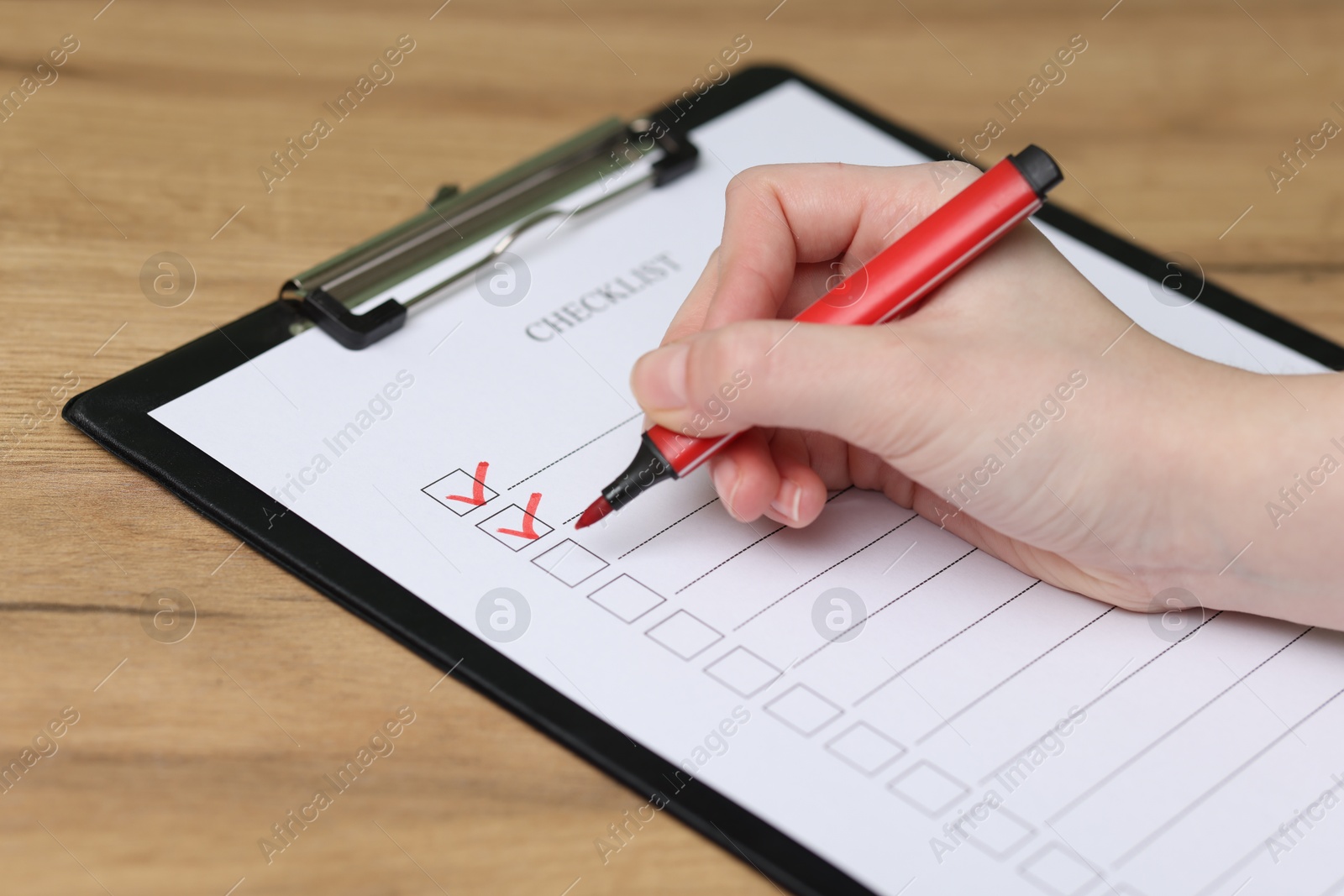 Photo of Woman filling Checklist with marker at wooden table, closeup