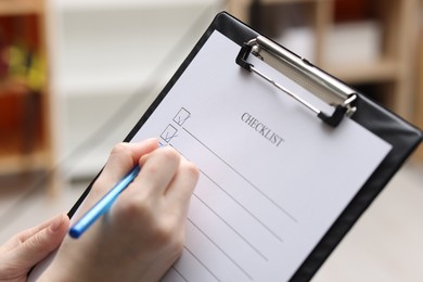 Photo of Woman filling Checklist with pen indoors, closeup