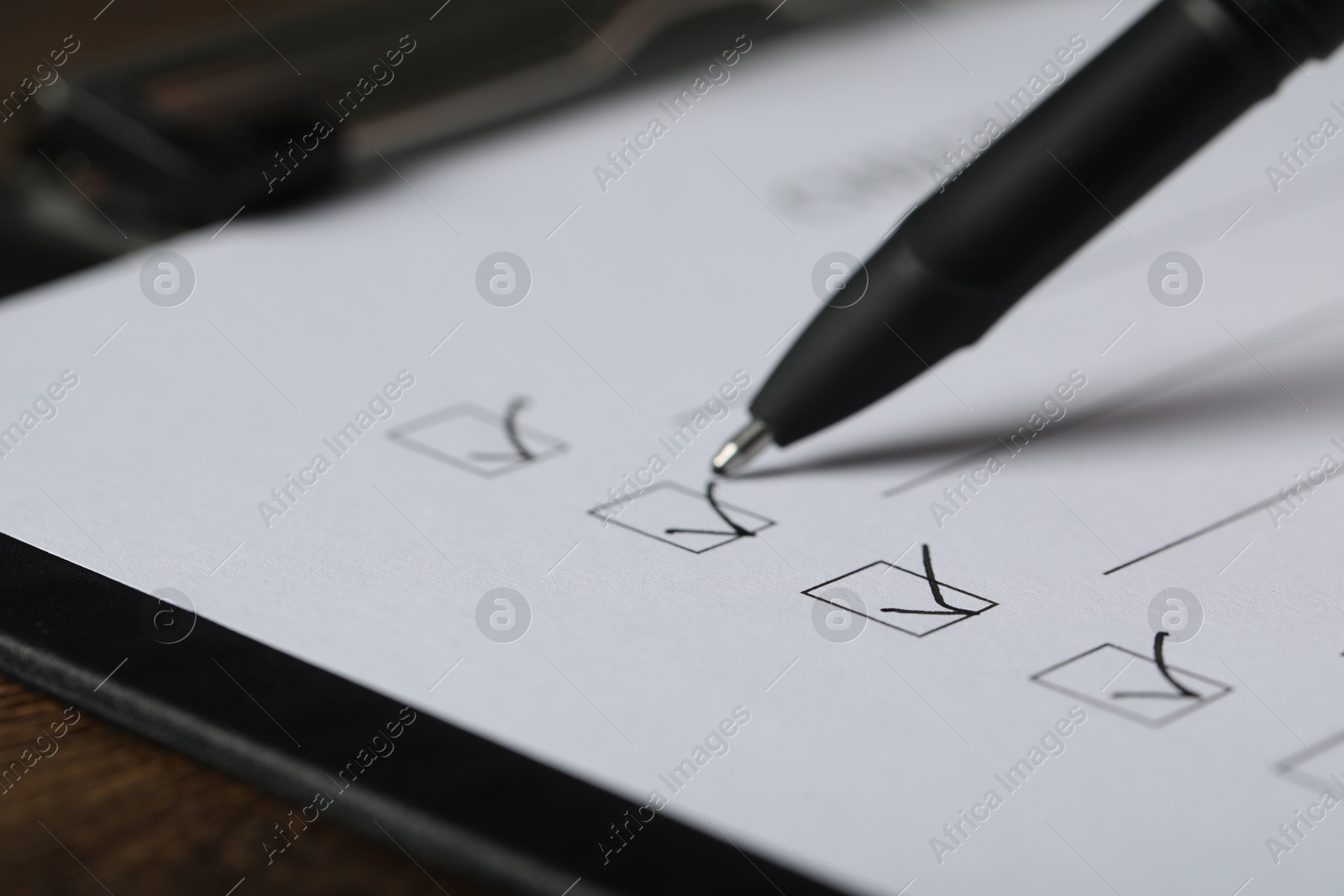 Photo of Paper sheet with checkboxes and pen at table, closeup