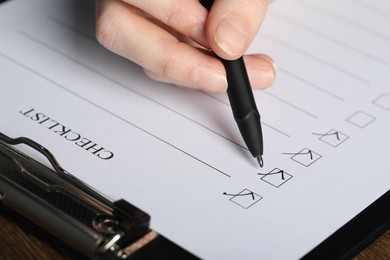 Photo of Woman filling Checklist with pen at table, closeup