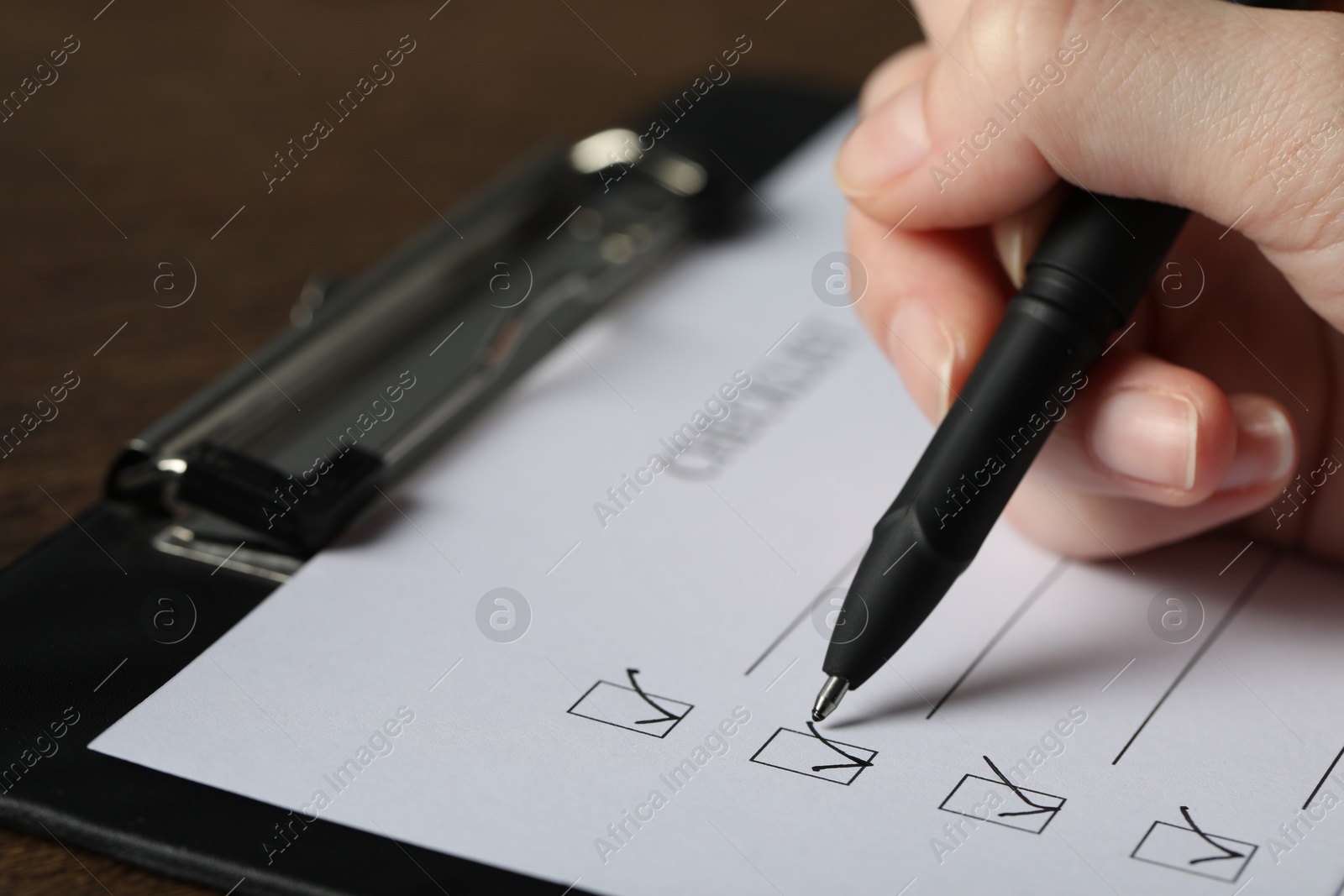 Photo of Woman filling Checklist with pen at table, closeup