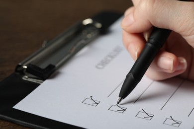 Photo of Woman filling Checklist with pen at table, closeup