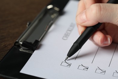 Photo of Woman filling Checklist with pen at table, closeup