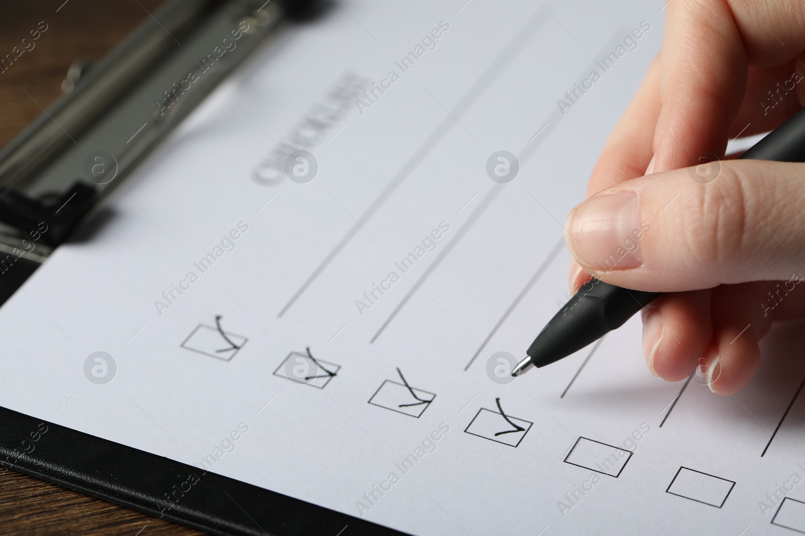 Photo of Woman filling Checklist with pen at table, closeup