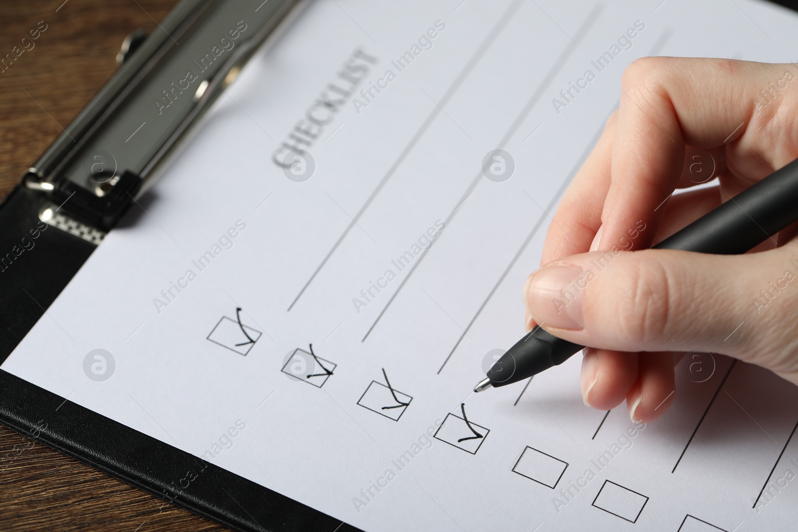 Photo of Woman filling Checklist with pen at table, closeup