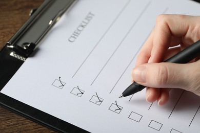 Photo of Woman filling Checklist with pen at table, closeup