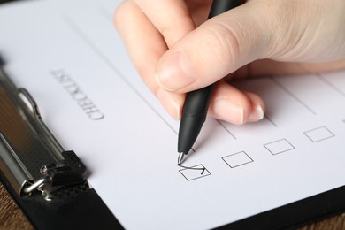 Photo of Woman checking box of Checklist at table, closeup