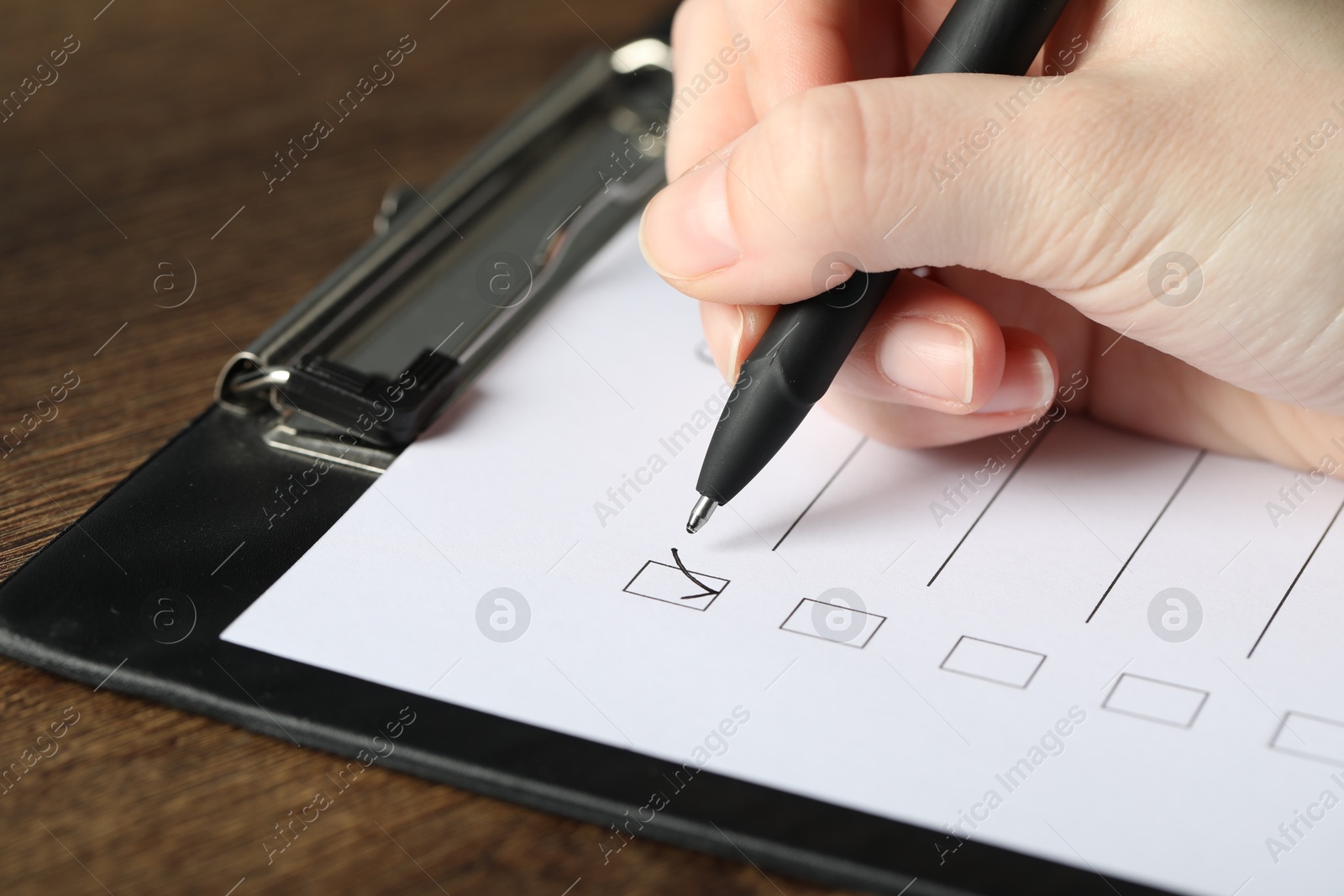 Photo of Woman checking box of paper form at wooden table, closeup