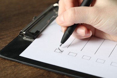 Photo of Woman checking box of paper form at wooden table, closeup