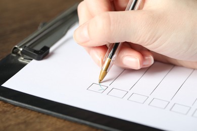 Photo of Woman checking box of paper form at table, closeup