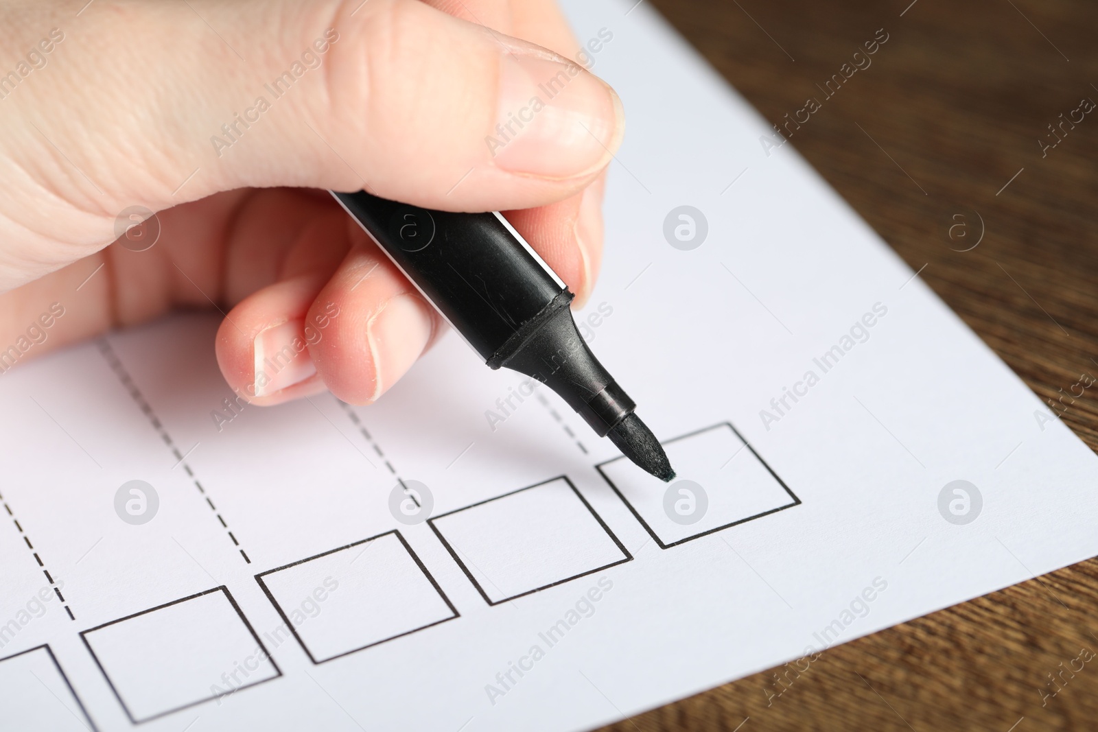 Photo of Woman checking box of paper form at wooden table, closeup