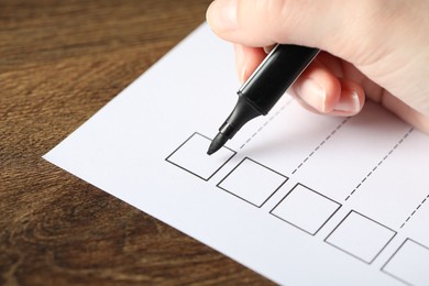 Photo of Woman checking box of paper form at wooden table, closeup