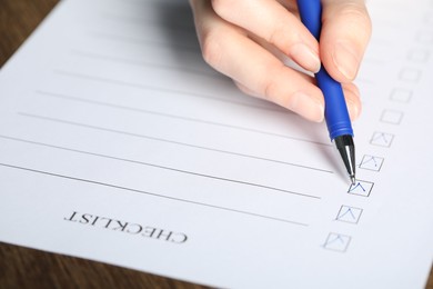 Photo of Woman filling Checklist with pen at table, closeup